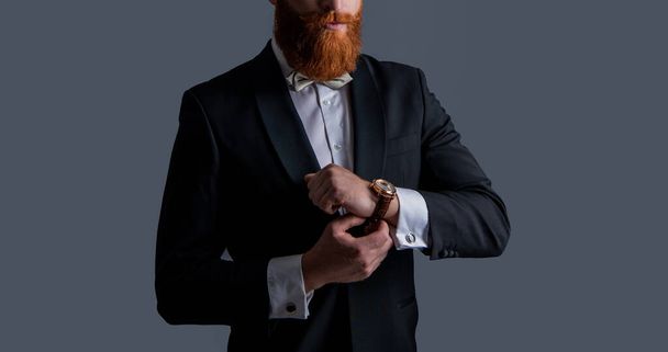 tuxedo fashion. cropped view of bearded man in tuxedo with wrist watch isolated on grey background. man studio shot in tuxedo and wrist watch. man wearing elegant wrist watch and tuxedo. - Фото, изображение