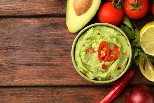 Bowl of delicious guacamole and ingredients on wooden table, flat lay. Space for text - Foto, Imagem