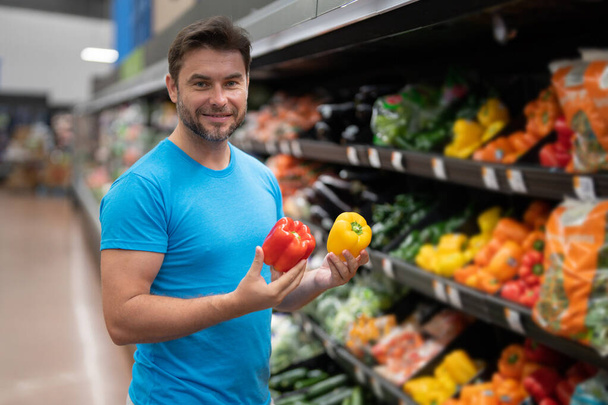 Portrait of man with shopping cart full of fresh vegetables in a food store. Supermarket shopping and grocery shop concept. Guy buying grocery in supermarket hold shopping basket - Foto, immagini