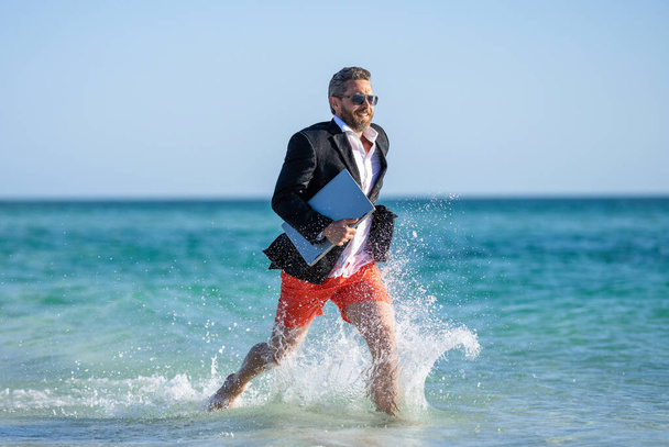 business success of successful businessman in wet suit with computer running in sea beach at summer vacation. - Fotoğraf, Görsel