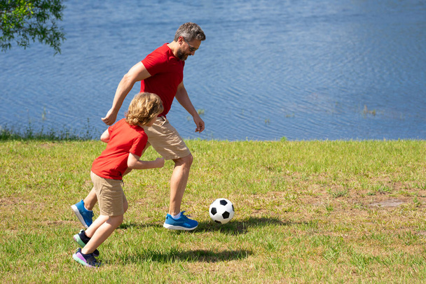 Father and son enjoy a friendly game of football. Practice passing and kicking soccer ball. Father teaches his son play football. Family sporty teamwork. Fathers day. Father teaches son play football - Fotoğraf, Görsel