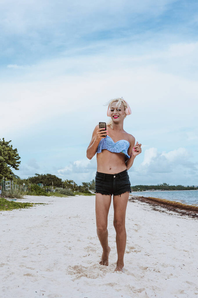 latin transgender donna ascoltare musica con cuffie e telefono cellulare in spiaggia in Messico America Latina, ispanica comunità lgbt - Foto, immagini