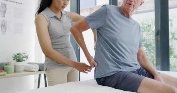 Physiotherapist, elderly man and back pain with consulting and medical support in a clinic. Physical therapy, senior patient and woman doctor with injury check in healthcare consultation and wellness. - Footage, Video