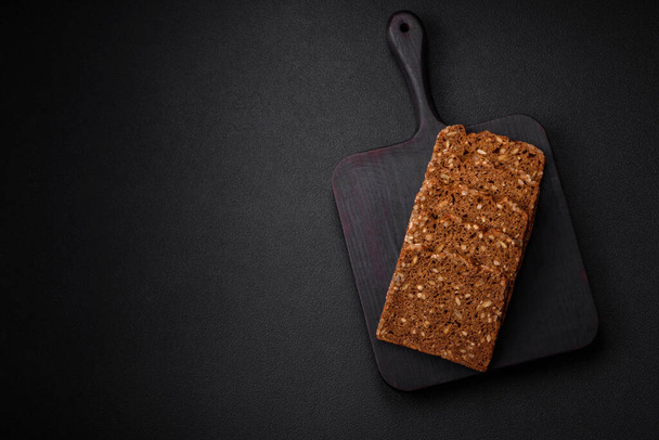 Délicieux pain brun croustillant frais avec des graines et des grains coupés en tranches sur un fond de béton foncé - Photo, image