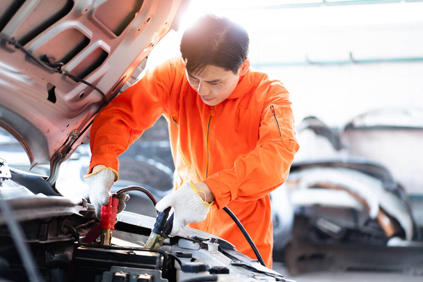Professional roadside technician support using an emergency jump start cable to connect a battery from other car to the one which out of battery. Car technician charging a dead battery in the old vehicle. - 写真・画像