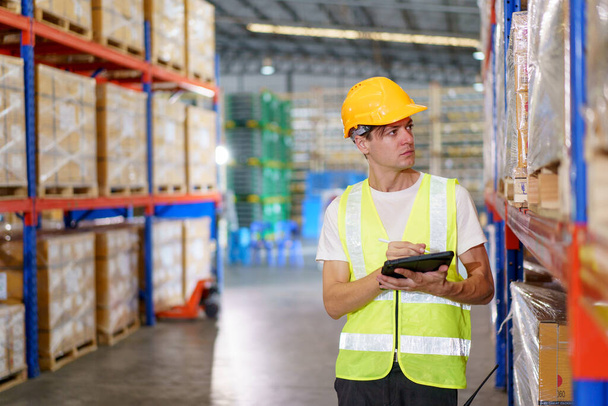 Happy cheerful caucasian white male warehouse worker checking an items or stock inventory in warehouse. Professional occupation in logistic industrial concept. - Фото, изображение