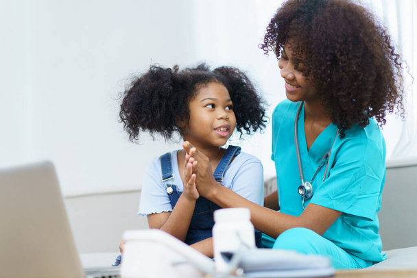 African American ethnicity female doctor and little girl in hospital, pediatrician taking to a little girl who laying down on the bed or sofa in hospital to talk about her sickness. - Foto, Imagen