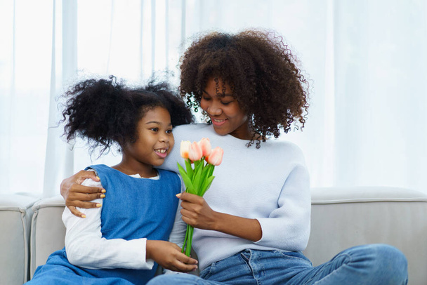 Lovely cute little girl gives her mother a beautiful bouquet of flower in the international Mother's Day, American - African black ethnic family portrait. International Mother's Day concept. - Photo, image