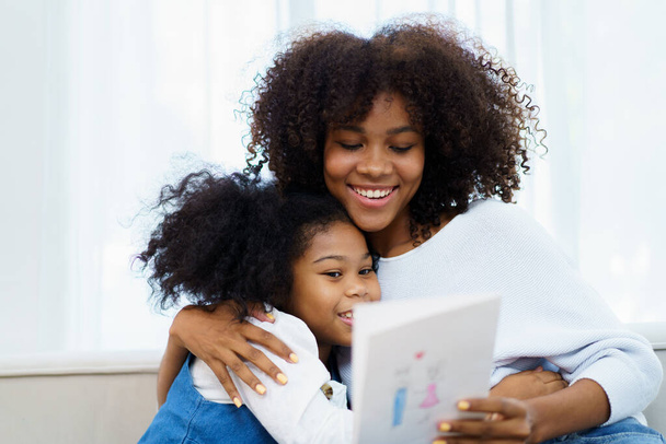 Lovely cute little girl gives mother her drawing post card in the international Mother's Day, American - African black ethnic family portrait. International Mother's Day concept. - Photo, image