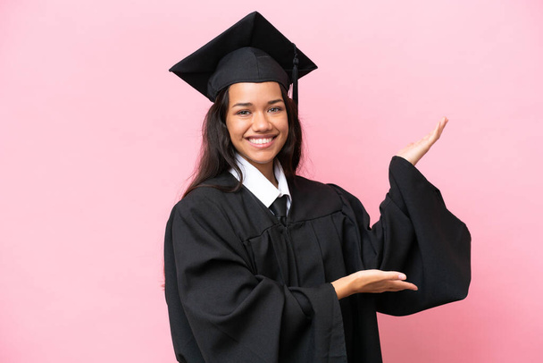 Young university Colombian woman graduate isolated on pink background extending hands to the side for inviting to come - 写真・画像