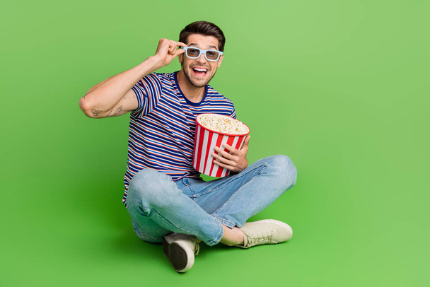 Full length photo of funky handsome man dressed striped t-shirt enjoying pop corm empty space isolated green color background. - 写真・画像
