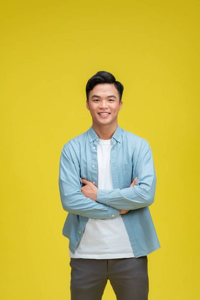 Confident young asian man standing cross arms against yellow background - Fotografie, Obrázek