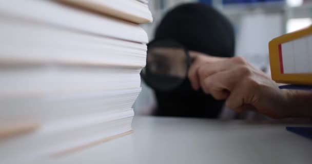 A woman in a balaclava looks at documents through magnifying glass. Fraud in business, theft intellectual property - Imágenes, Vídeo