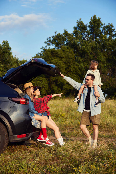 Stylish young family, man and woman going hiking with their children on warm summer evening. Travellers. Nature landscape. Concept of leisure time, fun, nature, active lifestyle, family, travel - Zdjęcie, obraz