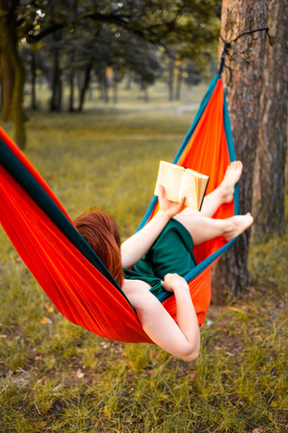 Young beautiful blonde girl in hammock reading book. Pretty woman leisure lifestyle portrait at nature ountdoor. Female relax in forest. Tourism in summer camp. Hobby - Foto, Imagen