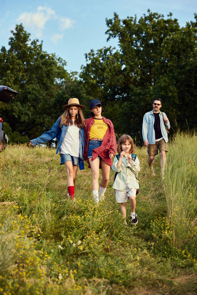 Young people, man and woman going hiking, walking with children on warm summer day. Beautiful nature scenery, fresh air. Concept of leisure time, fun, nature, active lifestyle, family, travel - Foto, Imagem