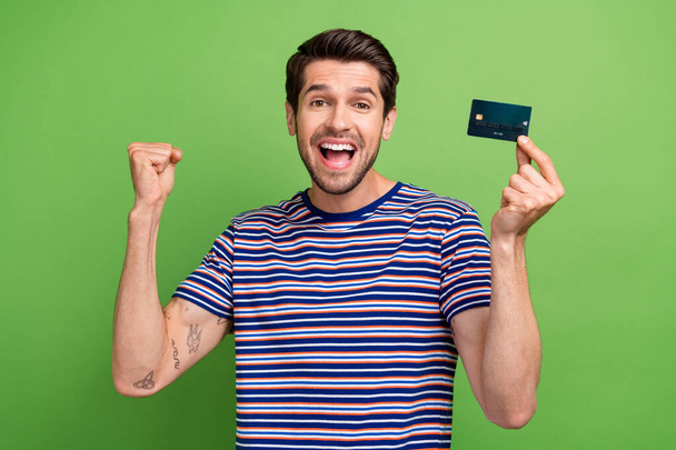 Photo of overjoyed funny young businessman successful entrepreneur premium wireless card fist up hooray isolated on green color background. - Foto, immagini