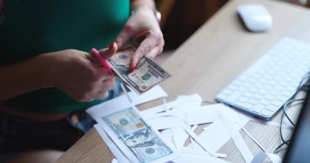 A woman sitting at a table cuts out fake dollars with scissors, close-up. Counterfeit money, fraud crime - Imágenes, Vídeo