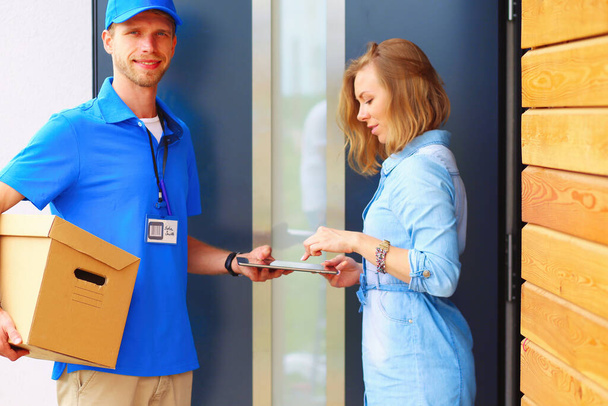 Smiling delivery man in blue uniform delivering parcel box to recipient - courier service concept. Smiling delivery man in blue uniform. - Foto, Bild