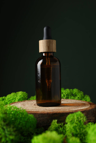 Мох, бутылка сыворотки на деревянном подставке, темно-зеленый фон - Фото, изображение