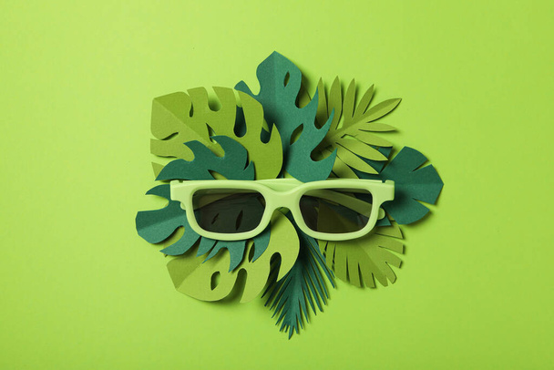 Light green sunglasses on tropical leaves on green background - 写真・画像