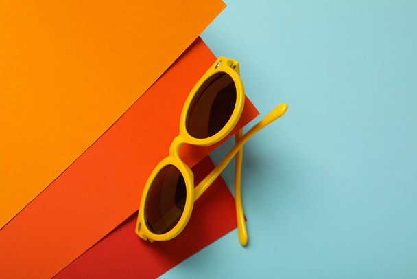 Orange sunglasses on red and orange paper on blue background, space for text - Φωτογραφία, εικόνα