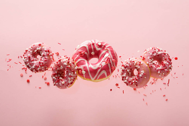 Falling pink donuts and sprinkles on pink background - Fotoğraf, Görsel