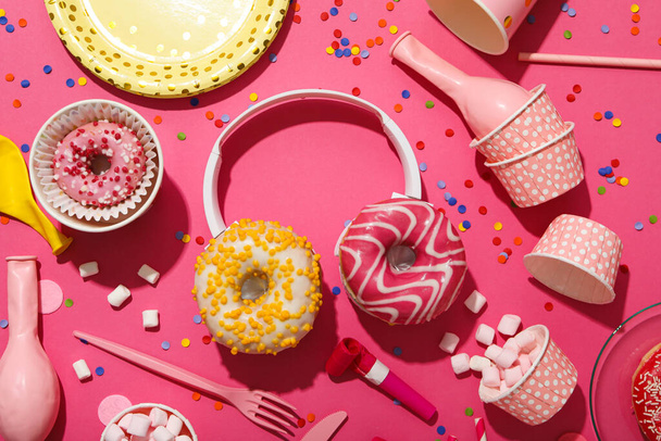 Donuts, fones de ouvido e suprimentos de festa em fundo rosa, vista superior - Foto, Imagem
