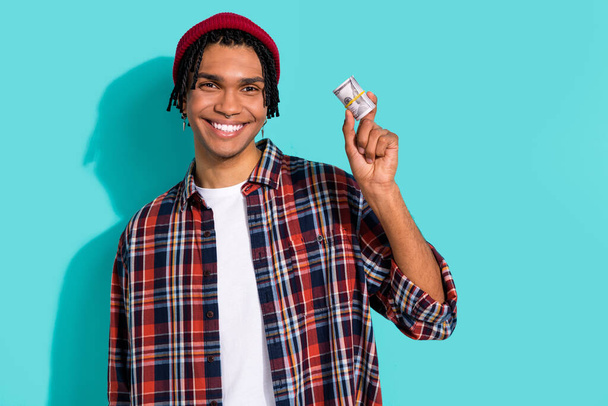 Photo portrait of nice young guy hold cash dollars money roll lottery dressed stylish checkered clothes isolated on cyan color background. - Foto, afbeelding