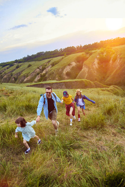 Parents going hiking with their children, daughters on warm summer evening. Beautiful hills landscape. Sunset. Concept of leisure time, fun, nature, active lifestyle, family, travel - Fotoğraf, Görsel