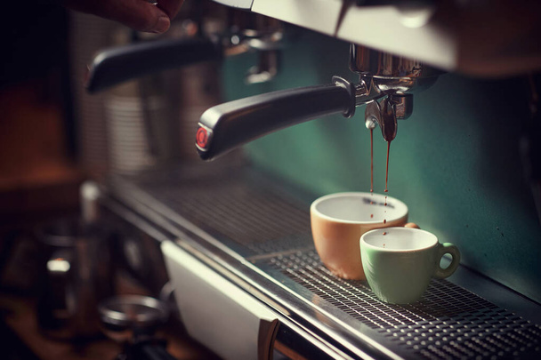 selective focus of espresso device, pouring jet of coffee into two cups. orange and green. - Valokuva, kuva