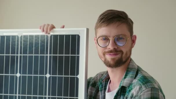 Close up portrait of cheerful man in casual clothes sitting next to solar panel and looking at camera - Footage, Video