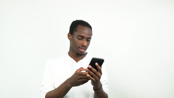 afro americano cara usando celular enquanto em pé no fundo branco - Filmagem, Vídeo