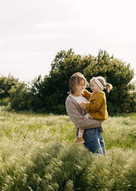 Mutter hält ihre kleine Tochter in den Armen, steht auf einem Feld mit hohem Gras. - Foto, Bild
