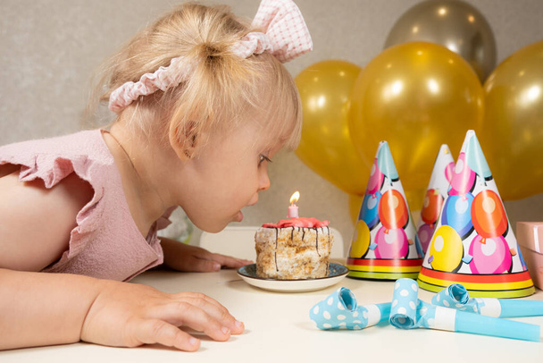 2歳の少女が誕生日ケーキにろうそくを吹き消し願い事をする. - 写真・画像