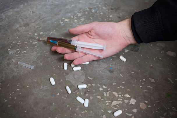 Addict hand with syringe and pills on the floor. International Drug Abuse Day. Addiction concept. - Фото, зображення