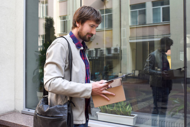 A bearded man with documents in his hands, against the backdrop of a modern building in the background. The concept of business failures and the problem of unemployment, laid off, crisis. - Foto, Imagen