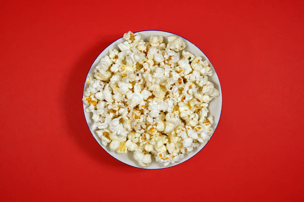 Popcorn in a plate on a red paper background. Close-up, top view. - Foto, Bild