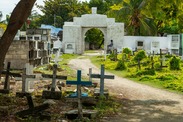 Cimetière catholique philippin atmosphérique, à côté de la mer du détroit de Cebu, tombes de la population locale décédée, disposées au hasard et partiellement ombragées par un arbre du soleil levant. - Photo, image