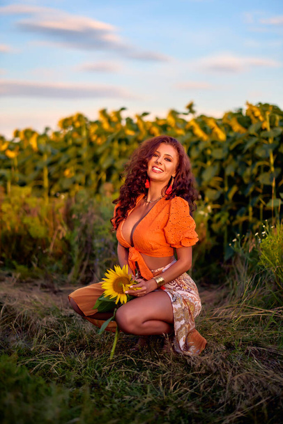 πορτρέτο μιας όμορφης γυναίκας κοντά σε ένα χωράφι με ηλιοτρόπια μια ηλιόλουστη μέρα στο ηλιοβασίλεμα. - Φωτογραφία, εικόνα