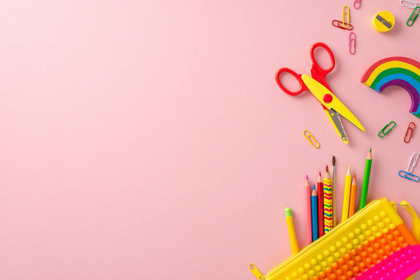 Scholastic essentials. Overhead shot of vibrant array: pop it pencil case, color pencils, paper clips, scissors, sharpener, rainbow plasticine. Spacious pastel background for text or advert - Foto, imagen