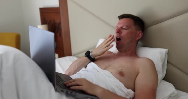 Nukkumaton nuori mies kärsii makuuhuoneessa kannettavan tietokoneen puutteesta. Freelancer ylitöitä ja ylitöitä - Materiaali, video
