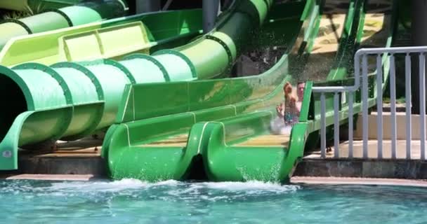人々は楽しみを持っており、男はウォーターパークでスライドを乗ります。プールでの観光客のための夏のエンターテイメント - 映像、動画