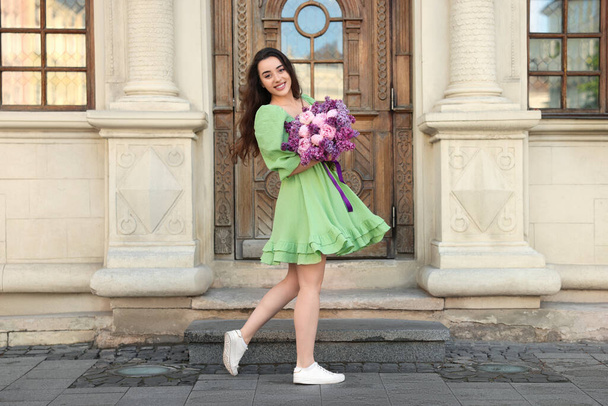 Beautiful woman with bouquet of spring flowers near building outdoors - Fotó, kép