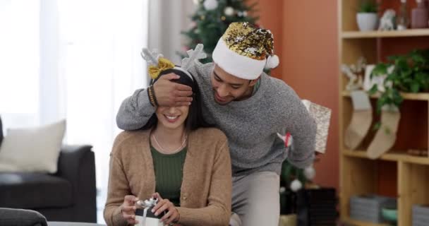 Χριστουγεννιάτικη έκπληξη, ζευγάρι και δώρο με τον άνθρωπο και γιορτή στο σπίτι με καπέλο κόμμα. Ευτυχισμένος, δίνοντας δώρα και νέους ανθρώπους με το παρόν, κουτί και επικοινωνία σε ένα σαλόνι για διακοπές με αγάπη. - Πλάνα, βίντεο