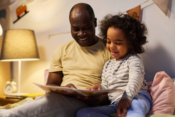 Счастливый папа показывает картинки в книге своему маленькому сыну, читая его перед сном ночью - Фото, изображение