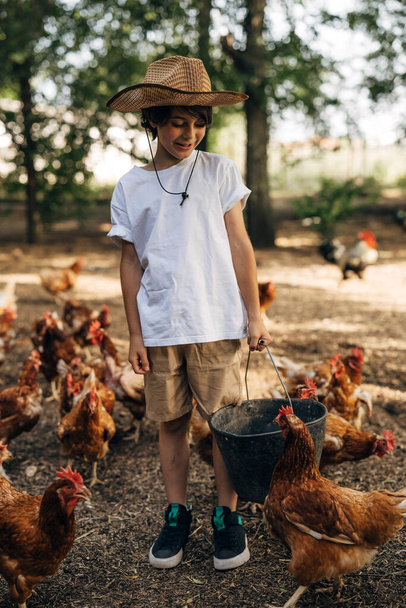 Happy Caucasian boy feeding chickens in the outdoors. - Фото, зображення