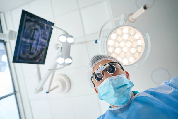 Man in special lenses and a medical uniform works in the operating room, the room is light and sterile - Fotoğraf, Görsel