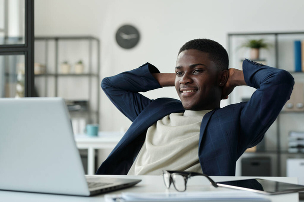 Молодой спокойный бизнесмен, держась за руки и глядя на экран ноутбука во время просмотра онлайн видео и наслаждаясь перерывом - Фото, изображение
