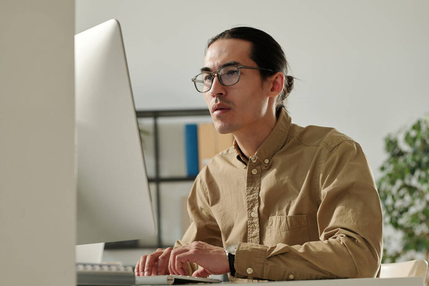 Молодой азиатский предприниматель-мужчина просматривает финансовые данные в Интернете на экране компьютера, анализируя их и готовясь к семинару - Фото, изображение